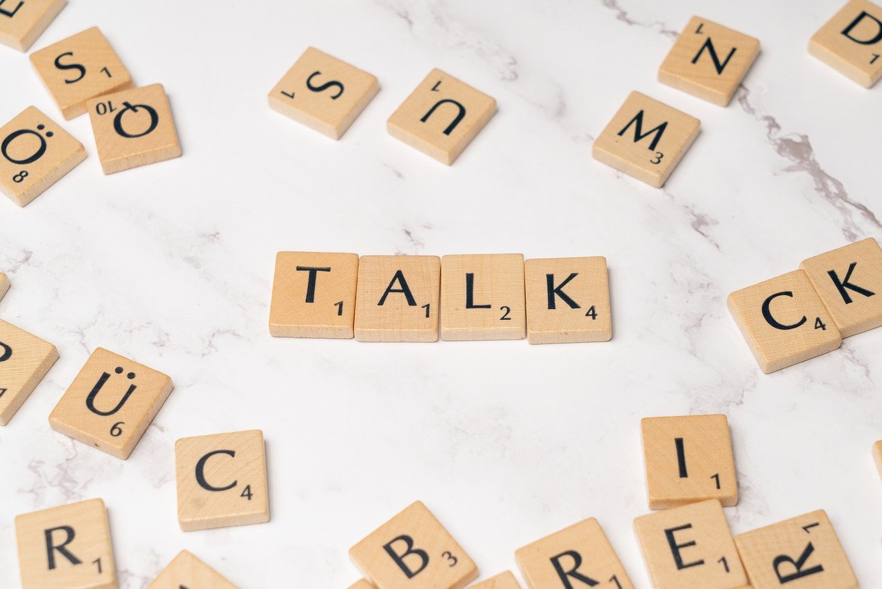 Scrabble tiles arranged to spell the word “TALK” on a marble surface.